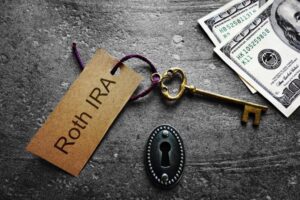 Roth IRA keychain on an old fashioned key and lock and money next to it.
