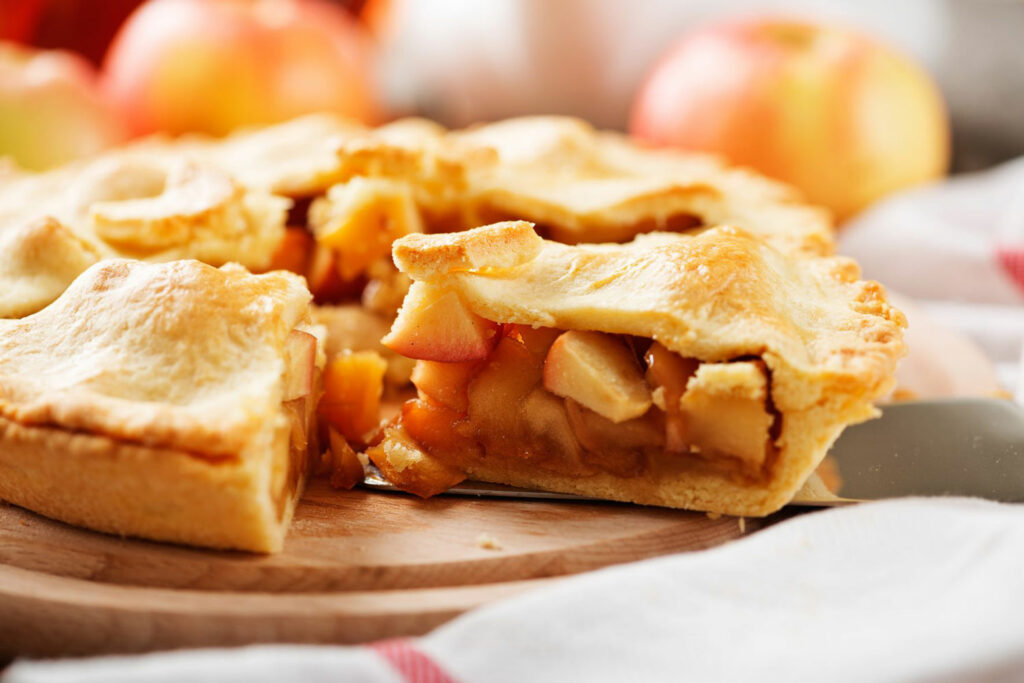 Delicious, warm apple pie made with a variety of apples with a piece missing.