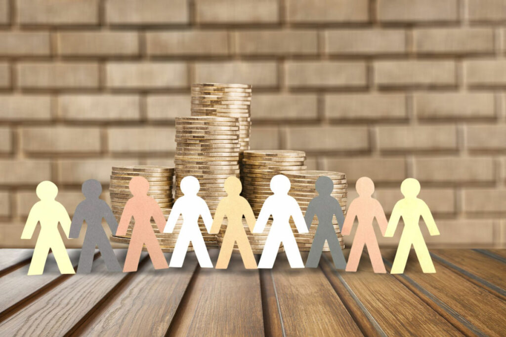 Paper cutout of people holding hands in front of a stack of coins to show the profitability of a crowdfunding investment opportunity.