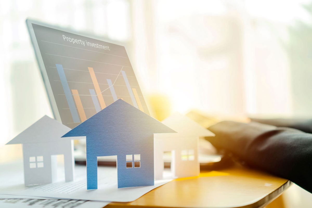 Paper houses in front of a laptop with “Property Investment” on the screen with an increasing graph to show investment growth after investing with a Self-Directed Real Estate IRA. 