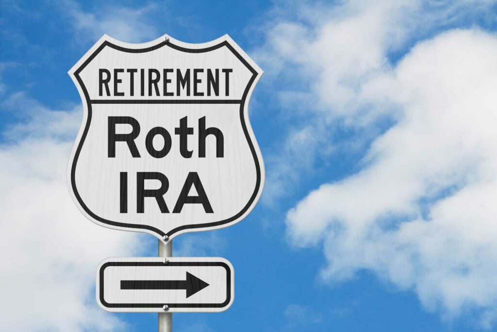 Blue sky and cloud background with street sign in front that says “Retirement: Roth IRA” and arrow pointing to the right.
