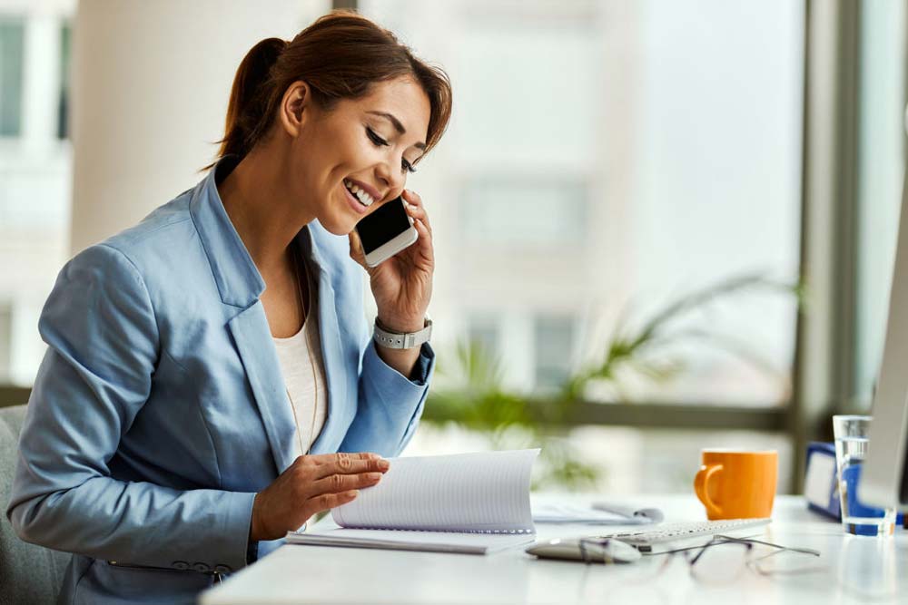 A happy investor woman at a table on the phone planning her retirement with her financial advisor.
