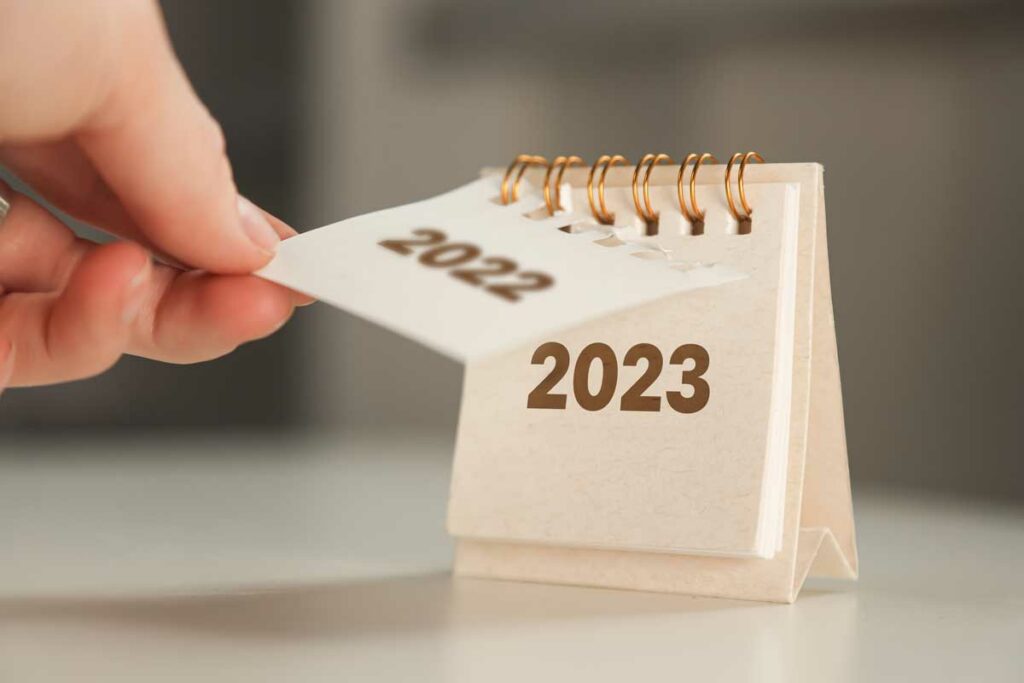 Hand turning a small calendar from 2022 to 2023, displaying the need for New Year’s resolutions for finance.