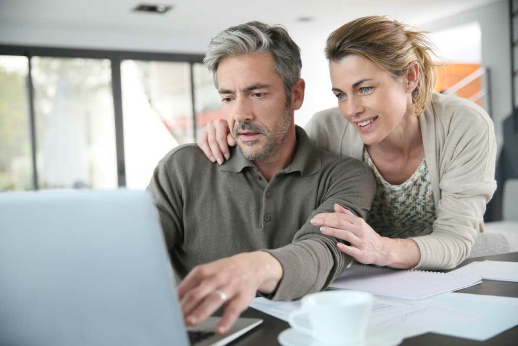 Middle-aged couple looking at a laptop with their finances and investments on it.