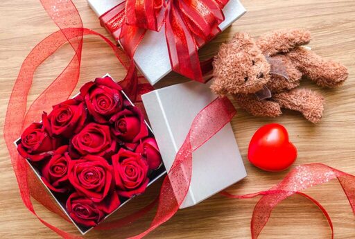 Valentine’s Day giftbox with red roses in it and a teddy bear next to it to display that is time to discuss finances with your sweetheart.