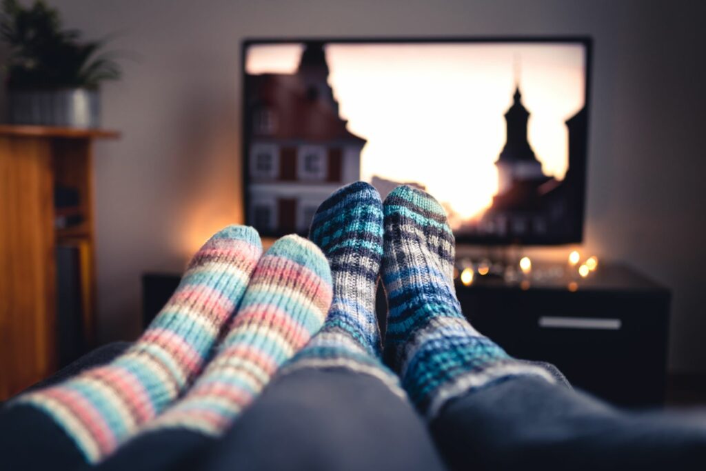 Two pairs of feet with cozy socks, cuddles up watching a movie in a candle-lit living room
