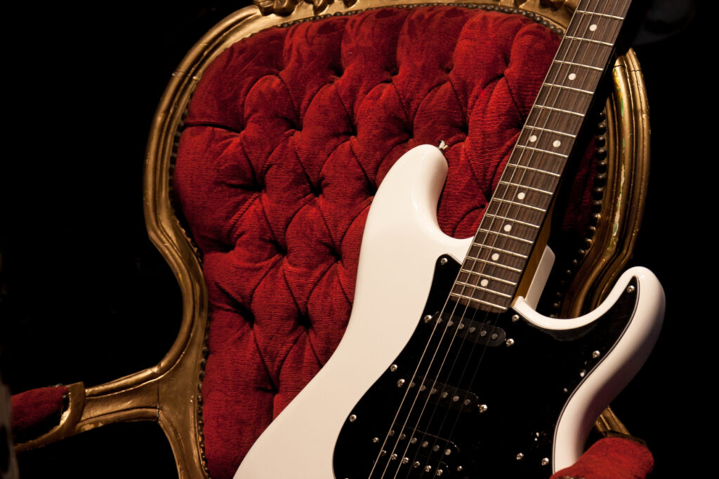 Electric guitar propped up on a red velvet, tufted chair