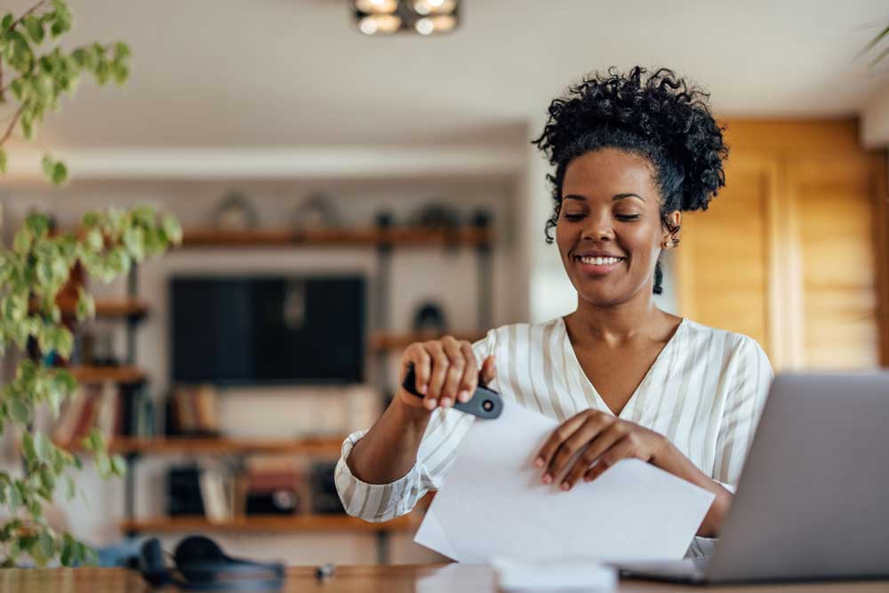 Self-Directed IRA account holder sitting at desk with a laptop and stapling papers together to indicate that setting up and managing a Self-Directed IRA is simple. 