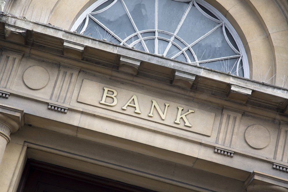 Outside of a bank building, to signify that when you invest in a promissory note, you essentially act as the bank and get to determine the loan terms and interest rates.