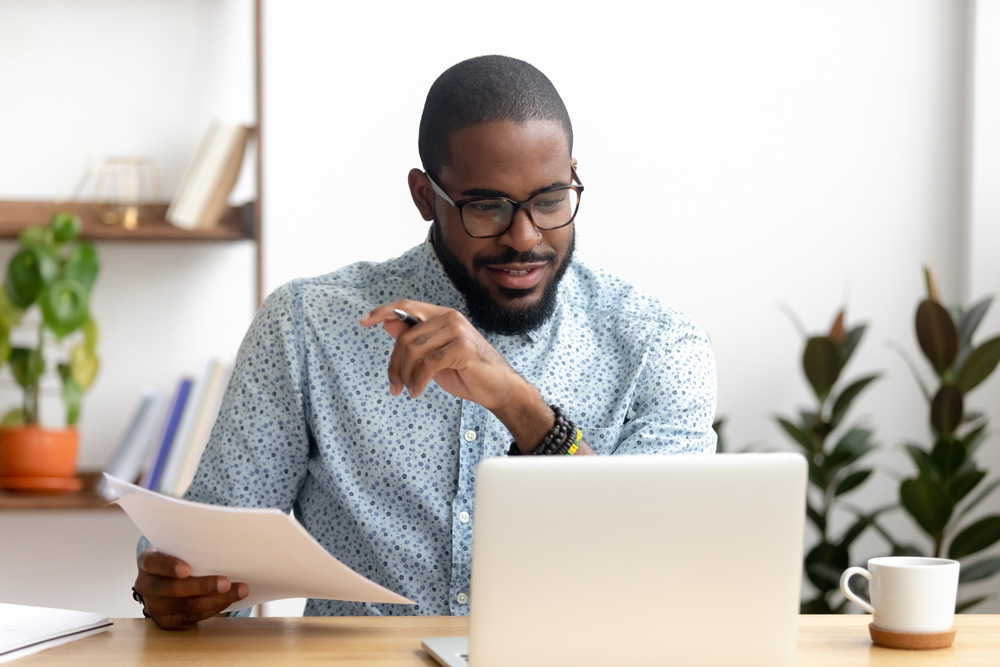 Directed Trust investor on a laptop and holding a piece of paperwork with plants in the background.