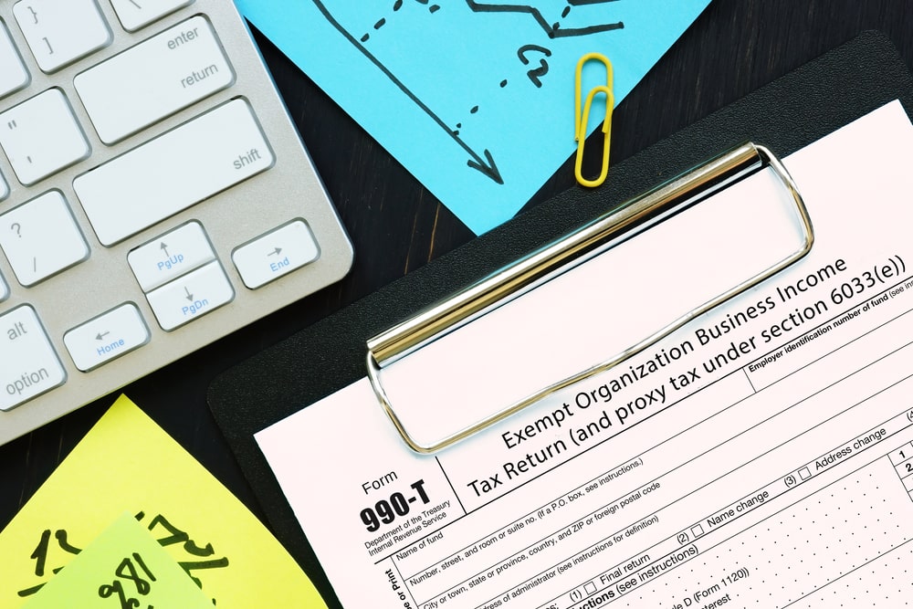 A Form 990-T attached to a clipboard on a desk with a paperclip and colorful post-it notes
