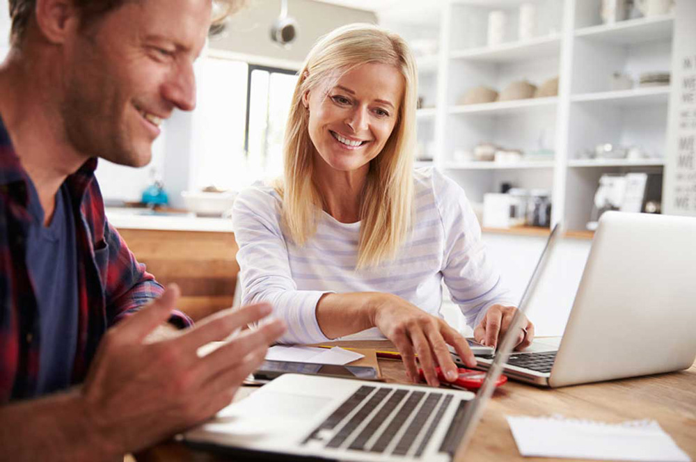 A smiling middle-aged couple looking at their laptops and opening a Self-Directed IRA so they can invest in real estate and grow their retirement savings.