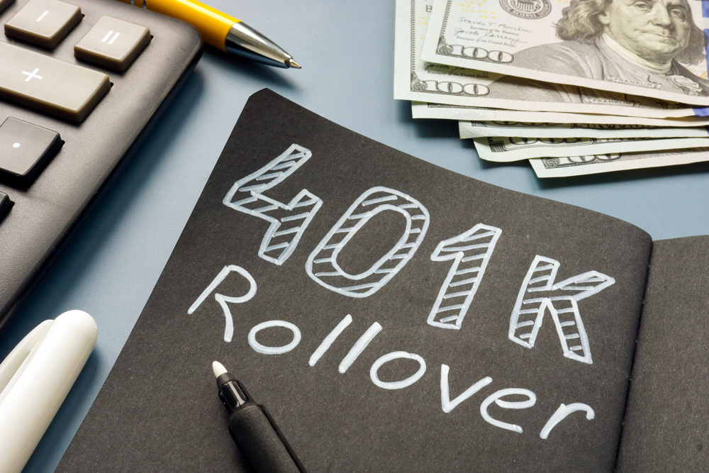 401(k) Rollover written in white ink on a black piece of paper with money above it.