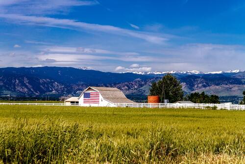 White barn with an American flag in an open field on a farm
