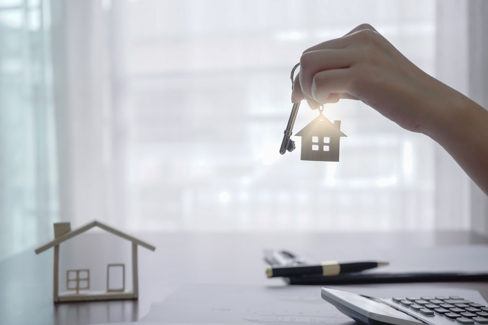 Hand holding a key to a real estate investment house, indicating that they bought real estate with an IRA.