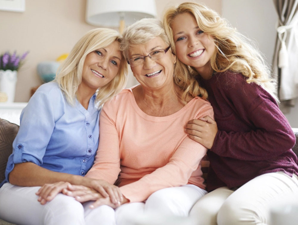 Three generations (grandmother, mother, and daughter) smiling because they have completed their legacy planning and designated their beneficiaries of their retirement account.