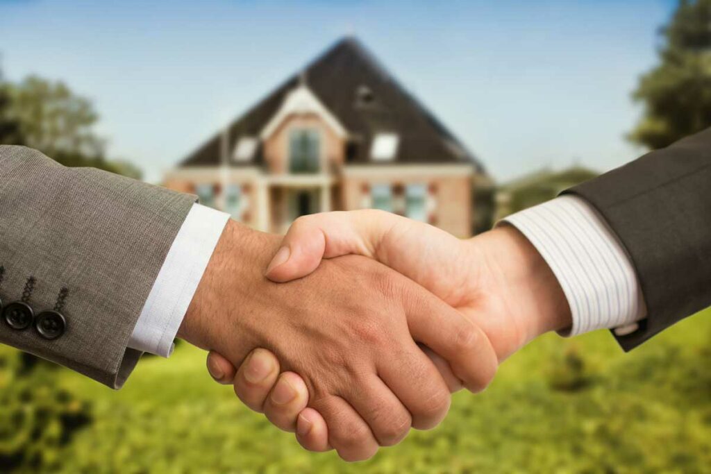 Two businessmen shaking hands in front of a real estate property, indicating that they have a note secured by real estate.  
