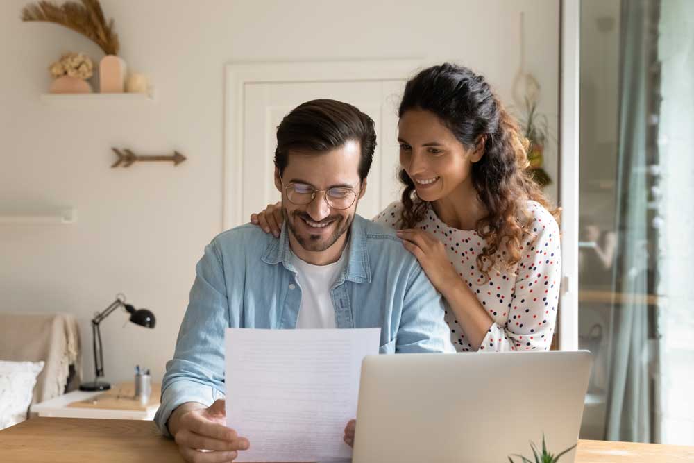 A couple looking at a paper and computer showing their retirement savings increase after they have created an investment strategy and successfully planned for retirement.
