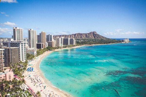Overlook of a Hawaii beach, tall buildings, and a mountain, displaying that you can invest with a Self-Directed IRA in Hawaii in assets like real estate, businesses, precious metals, and beyond.