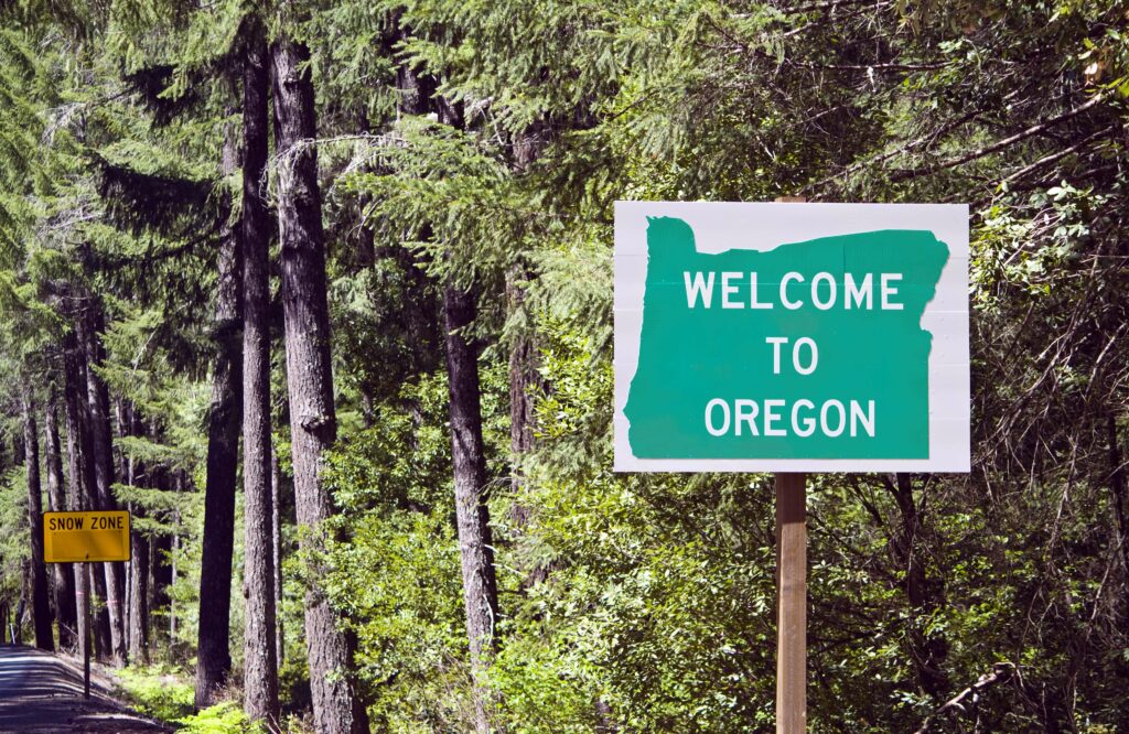 welcome to Oregon sign on the side of the road in the middle of the forest