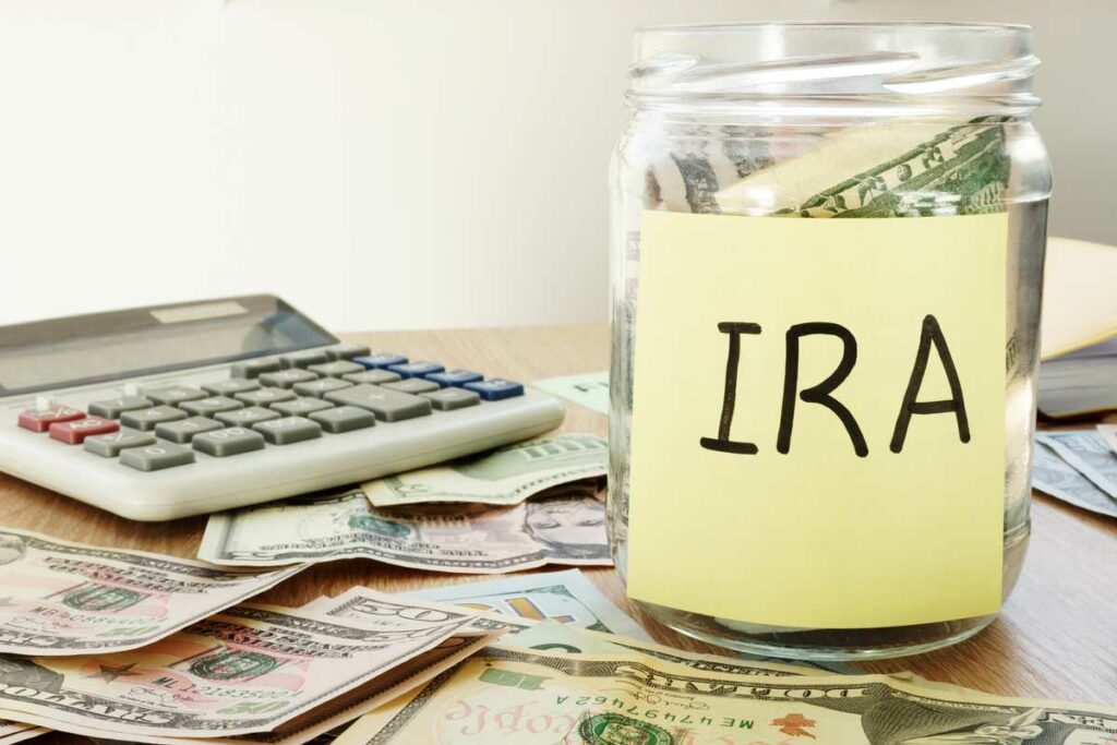 Mason jar labeled "IRA" with a calculator and money on the table to show the act of saving for retirement with a Self-Directed IRA.