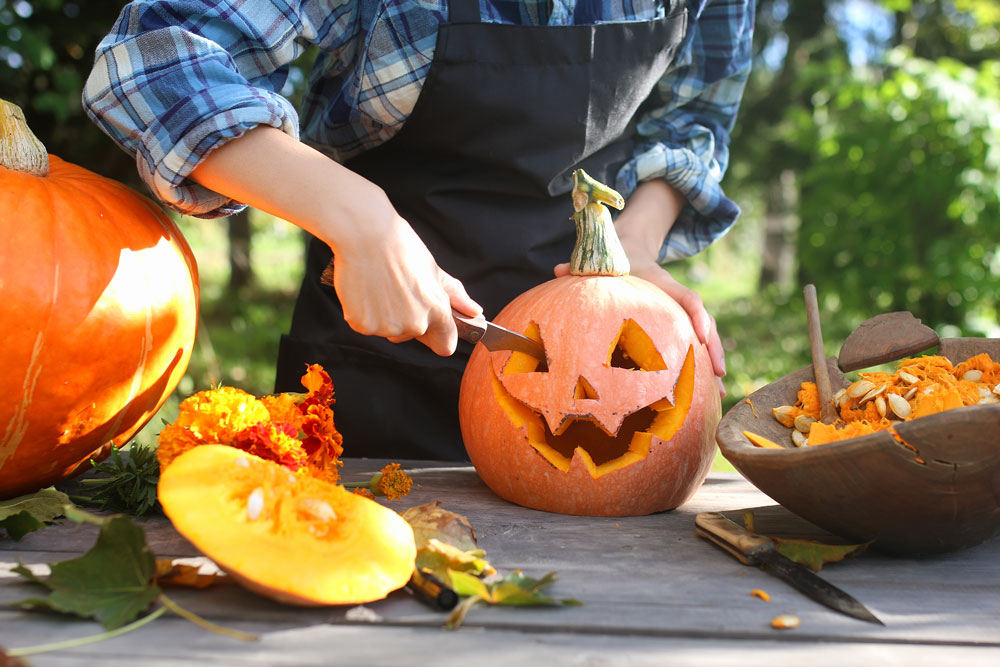 A person carving a pumpkin on a table with a knife in hand next to another pumpkin to show that carving a pumpkin and a Self-Directed IRA are similar.