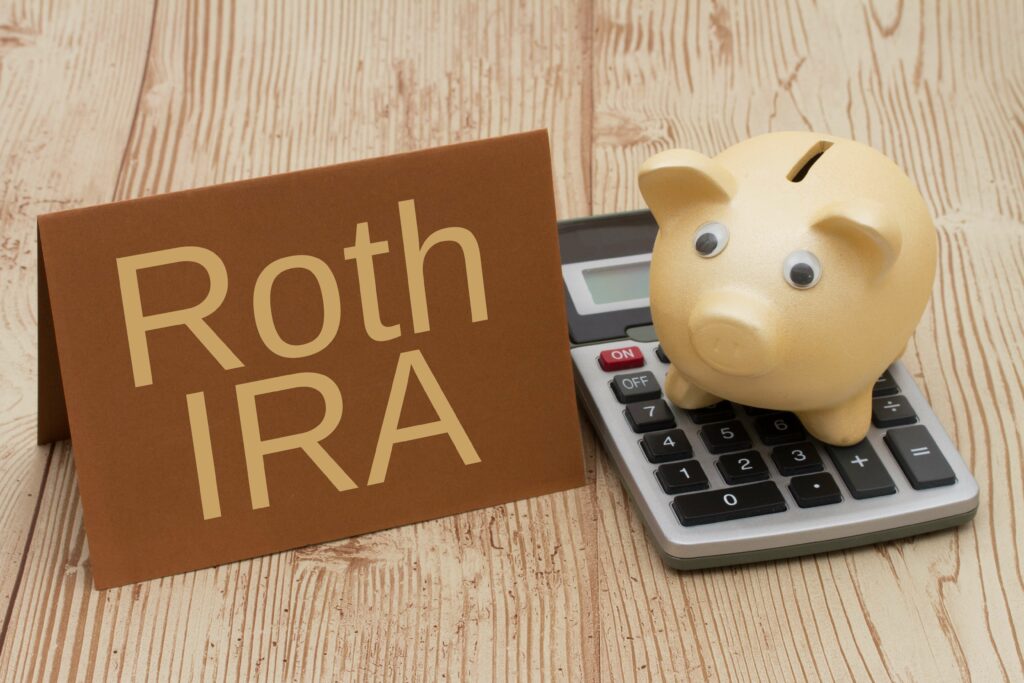 Roth IRA written on golden piggy bank, card and calculator on wood background