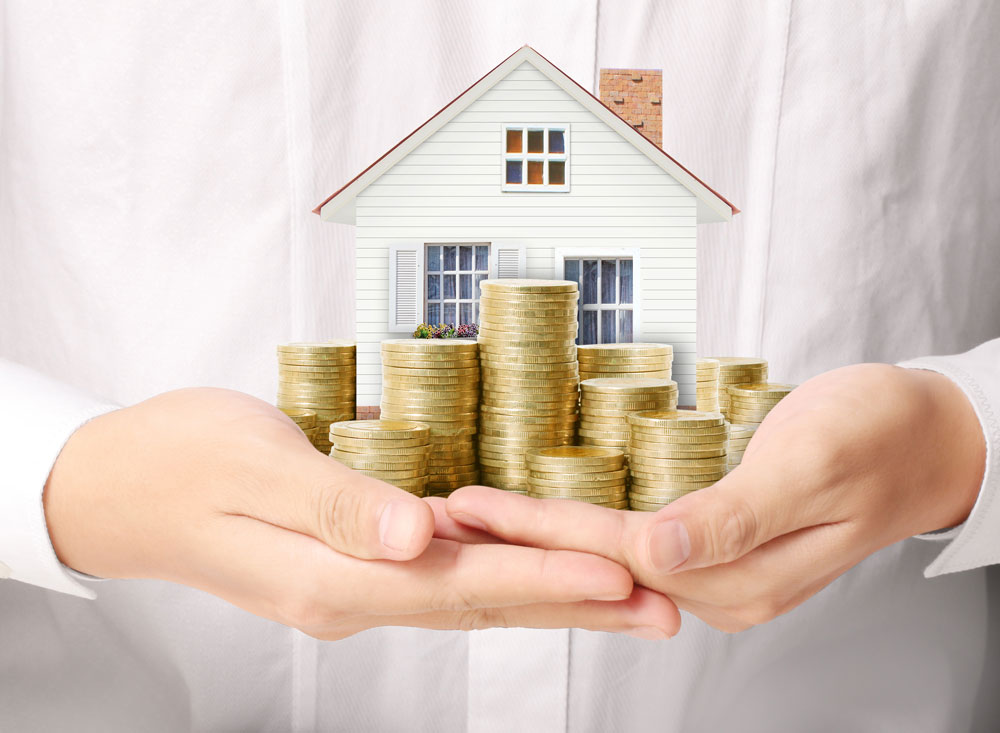 Investment Property IRA investor holding a miniature house with stacks of coins in front to display that you can invest in real estate with your retirement funds.