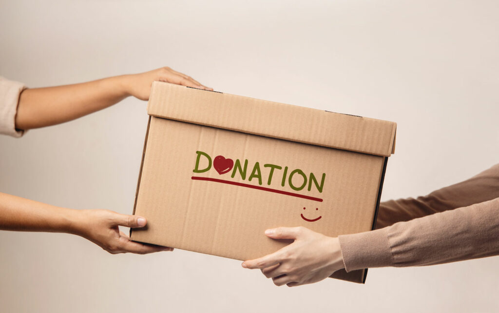 One person handing another person a box that says “Donation” on it, indicating a qualified charitable distribution from their Self-Directed IRA.