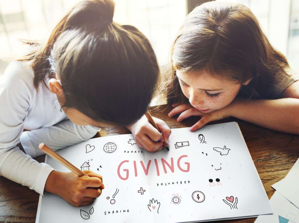 Two young girls filling in a coloring book all about giving and charity this Thanksgiving.
