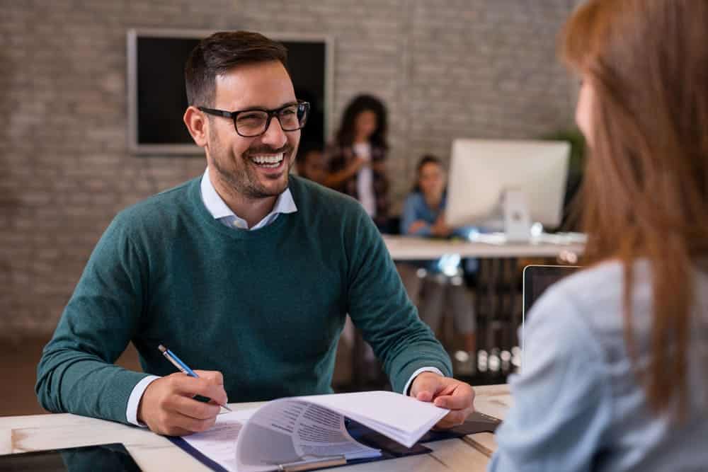 Investment Sponsor filling out paperwork and smiling talking to a knowledgeable Self-Directed IRA custodian.