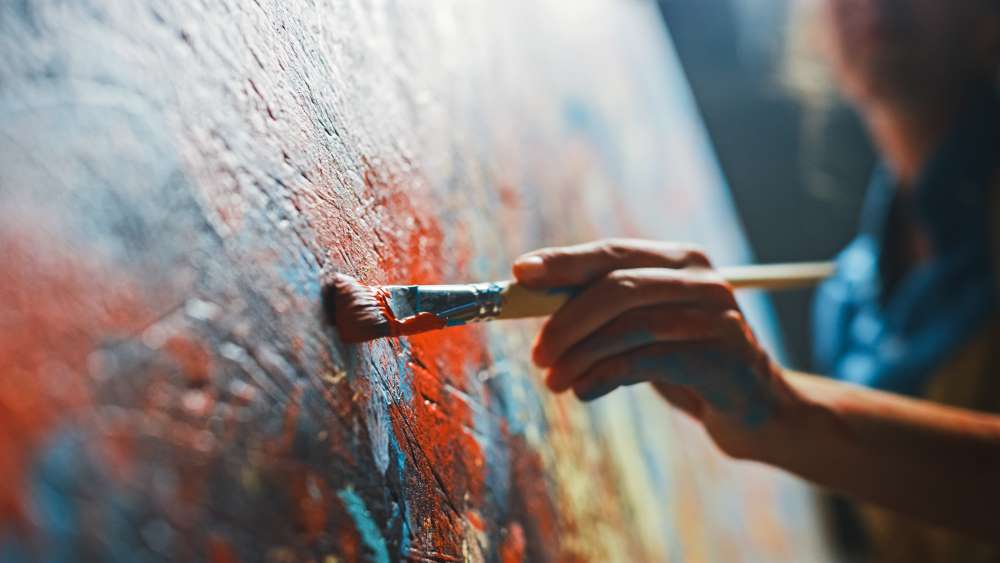 An artist strokes her paintbrush across an easel as she paints her abstract art.