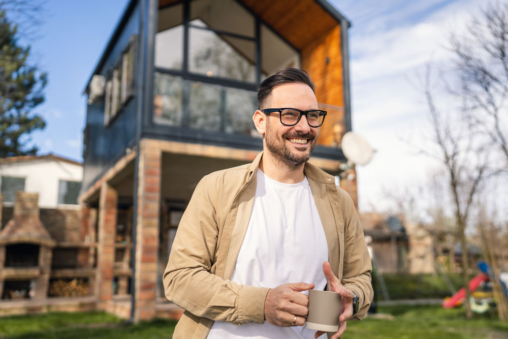 Real Estate IRA investor standing and smiling in front of a real estate investment property held in his Self-Directed IRA.