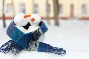 Two snowmen sit side-by-side, conjoined with a scarf, depicting how love and romance is still prevalent during the winter season.