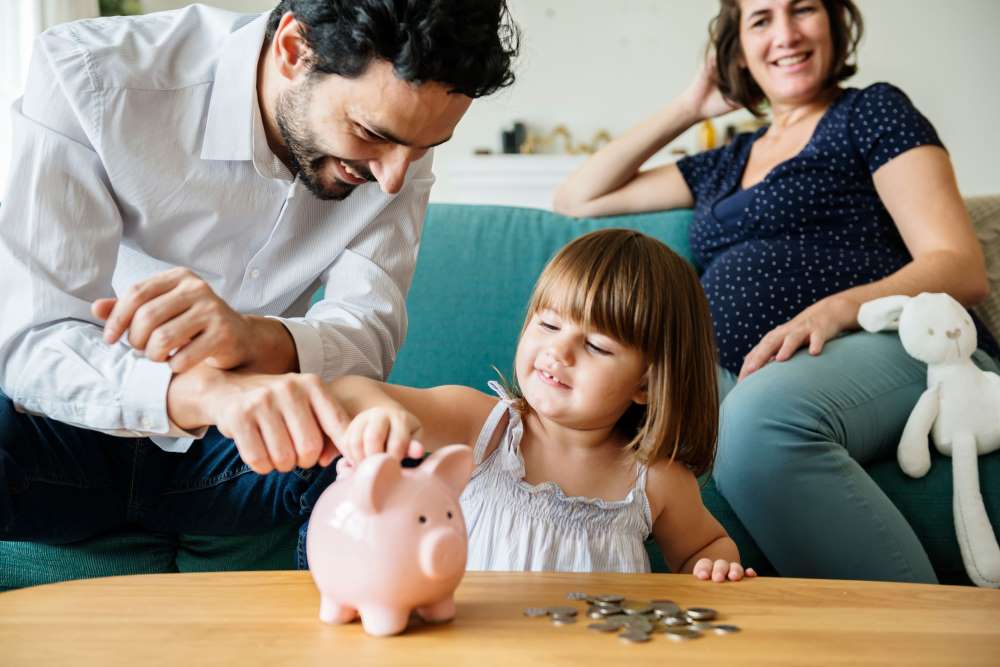 A family gathers around a piggy bank as they teach their child about the importance of spending and saving habits.