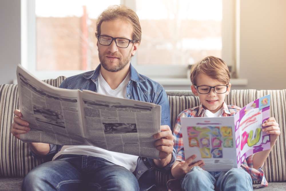 A father and son read the paper and a magazine side by side, instilling the importance of being mindful of asset trends, Custodial Self-Directed IRA, and financial literacy.