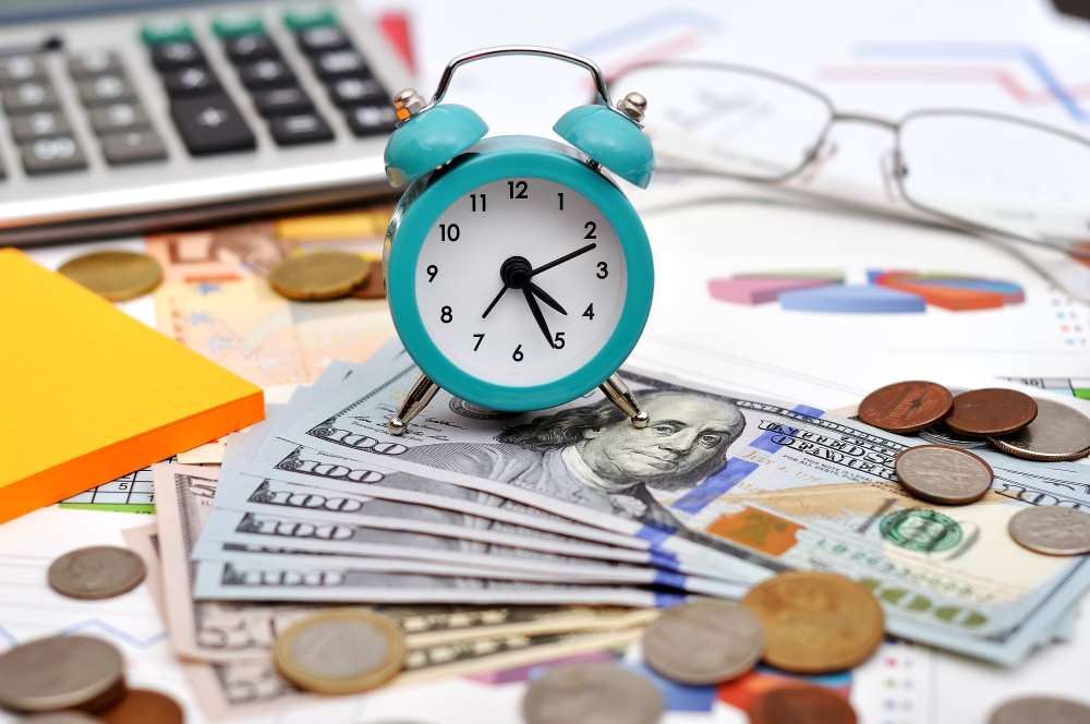 A clock, sitting on top of wads of cash and coins, showing how garnering Checkbook Control can allow you to purchase investments in real time and potentially increase your retirement savings through a Self-Directed IRA LLC.