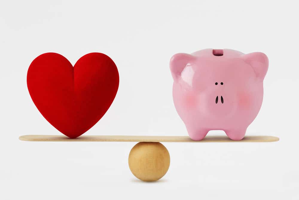 Balance board with a heart on one side and a piggy bank on another to show that alternative investments can hedge against stock market fluctuations.