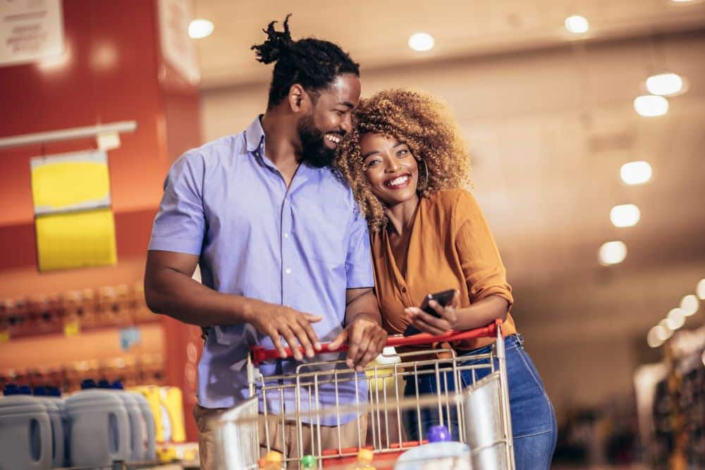 A happy couple pushes a shopping cart around the store, equally to how they would perform their due diligence and consider which alternative asset is best for their SDIRA before investing.
