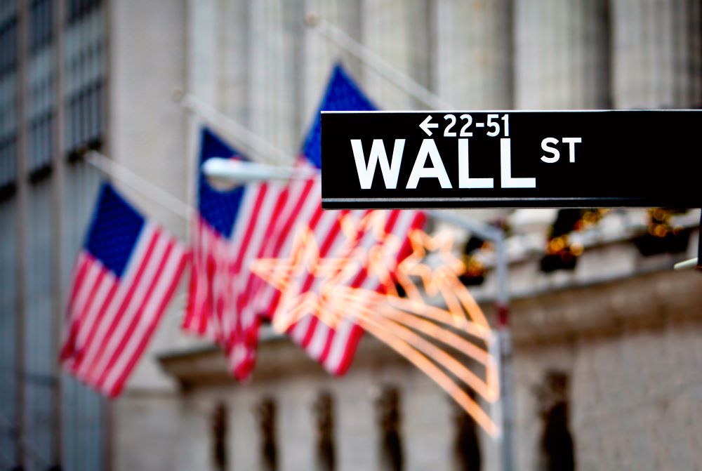 Wall St. street sign in New York City with American flags waving in the background.