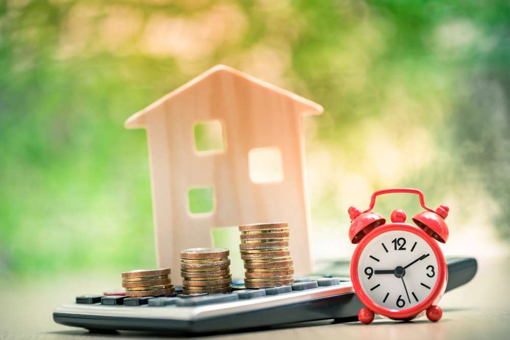 A wooden house with stacked coins and a clock, identifying that a real estate investment takes time, but typically produces in earnings.