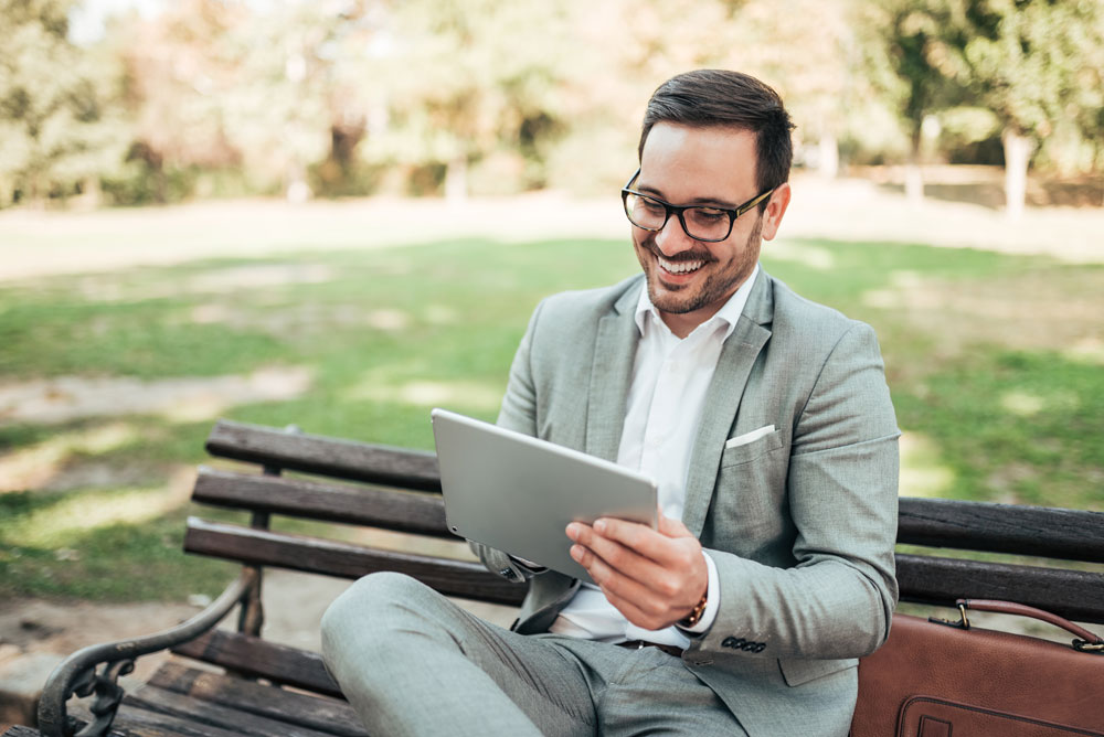 Investment Sponsor on a bench in a park looking at a tablet, researching Self-Directed IRA custodians.